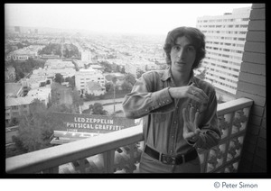 Rock journalist Stephen Davis on the balcony of Robert Plant's room at the Riot House, with a billboard in the background advertising Led Zeppelin's album Physical Graffiti