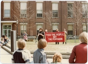 Gina Ayvazian speaking at a Nuclear Freeze demonstration, in front of a banner reading 'Feed the people, not the Pentagon'