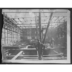 Workers stand inside building frame with partially constructed walls with windows