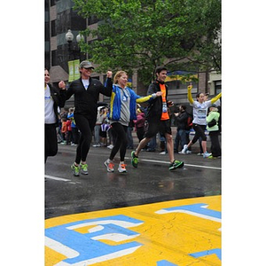 Five runners approach the "One Run" finish line at Copley Square; four smiling and holding hands