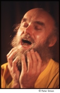 Ram Dass with his hands on his beard, on stage with Amazing Grace