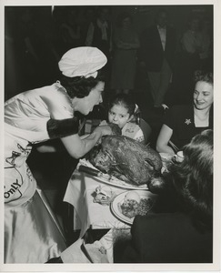 Woman in chef's hat feeding turkey to child in wheelchair