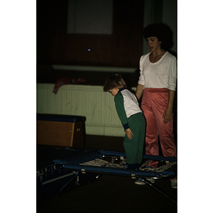 Child standing on trampoline, with a woman watching nearby