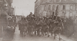 Soldiers of the 106th Regiment with bayonets march through a street lined with civilians, Châlons