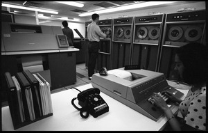 Computer room scene: woman at the console of a Honeywell Model 400 mainframe, with printer and card reader (?) in background