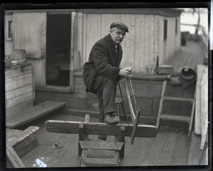 Capt. Fred Hutchins of Bucksport, who was tied up with his wife in houseboat at South Station: Hutchins with a bucksaw