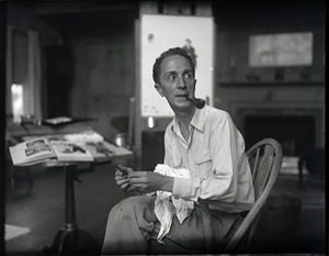 Norman Rockwell seated in a Windsor chair in his studio, holding a paintbrush