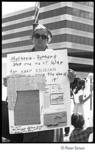 Protester at a Mobilization for Survival antinuclear demonstration near Draper Laboratory, MIT, with sign reading 'Mothers - Fathers stop the next war for your children'