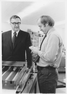 Dr. Dee Edington standing indoors demonstrating rat exercise apparatus