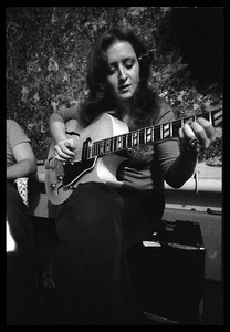 Bonnie Raitt seated backstage, playing guitar