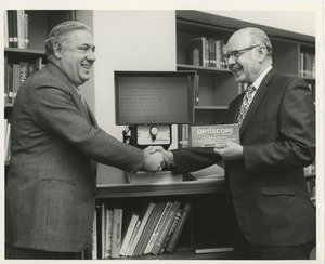 Two men shaking hands in front of an optiscope enlarger