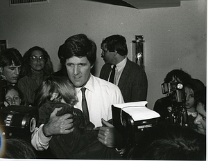 John Kerry holding unidentified child while surrounded by press