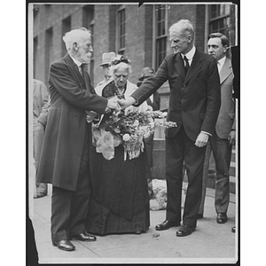 Two men hold hands at George Meserve Tribute in front of woman holding a bouquet of flowers