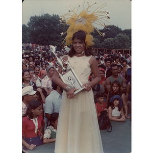 A girl wears a large headdress and carries a trophy at the Festival Puertorriqueño