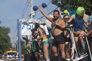 Parade marchers waving from atop a float, holding a blue dumbell : Provincetown Carnival parade