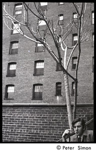 Joe Pilati seated by an urban tree, smoking a cigarette