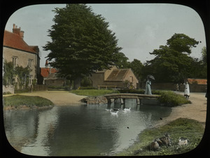 Country Village, Gloucestershire, England, FAW (woman on stone footbridge over brook with ducks, village in the background)