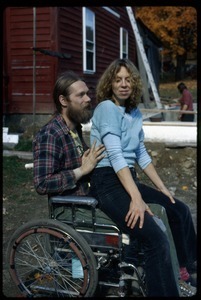 Karen Moreno seated in Peter Natti's lap in front of house, Montague Farm Commune