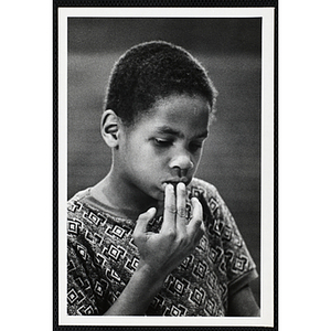 An African American boy from the Boys' Clubs of Boston looking down with his fingers on his lip