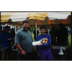 A man holding an envelope poses with another man during the Battle of Bunker Hill Road Race