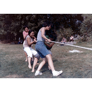 Four young women play tug-of-war, with two boys watching in the background