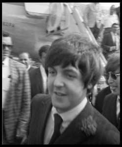 Paul McCartney after leaving the plane as the Beatles arrive at the airport, John Lennon in background