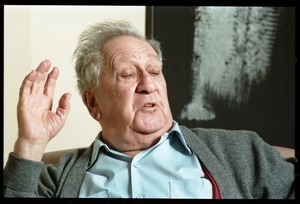 Fine art photographer Aaron Siskind: close-up portrait, gesturing, while seated in a armchair in his living room