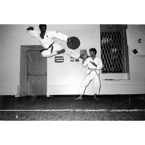 A Hispanic man demonstrates a karate flying side kick, while a male teenager blocks the kick