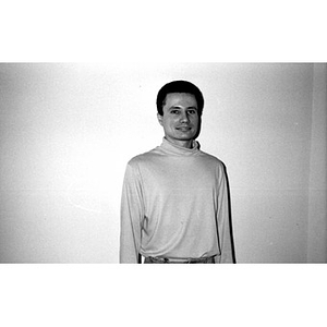 Portrait of a man in a turtleneck standing against a plain white wall.