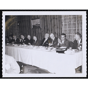 Several men, seated at a long table, eat and converse during the Kiwanis Club's Bunker Hill Postage Stamp Luncheon