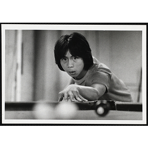 An Asian American boy from the Boys' Clubs of Boston aiming his cue at the cue ball