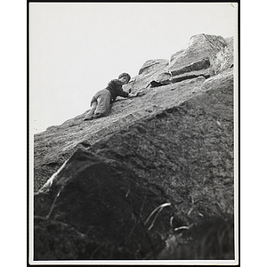 A boy climbs a rock with a rope harness