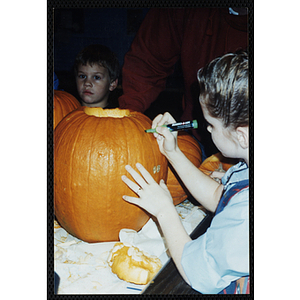 A girl marks a pumpkin for carving with a marker