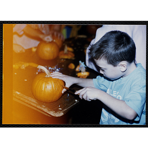A boy carves a pumpkin with a knife