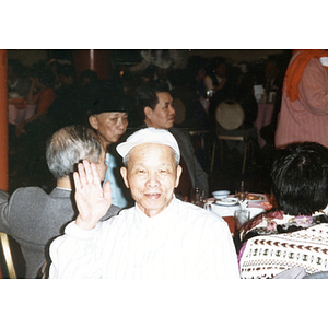 Man smiles at a Chinese Progressive Association dinner, with other members seated at tables around him