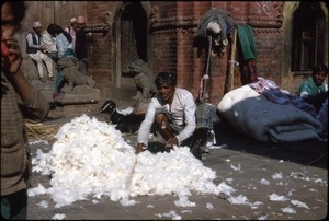 Man with bedding, mattresses, people, and goat behind him in square