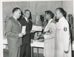 James Burrows presents a certificate of completion of training to a 1964 Prosthetics and Orthotics training graduate while two other men look on