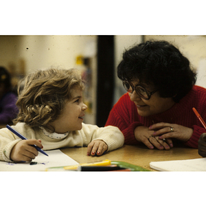 Young girl writing and looking at a woman