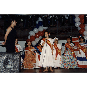 A girl speaks into a microphone on stage while other girls stand behind her at the Festival Puertorriqueño