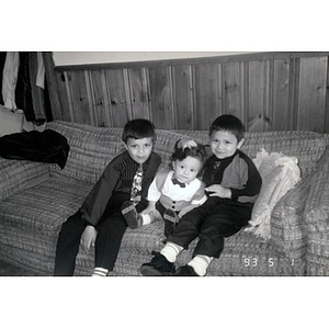 Two little boys and a toddler dressed up in their best sitting on a couch.