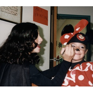 Woman painting a child's face to complete the Minnie Mouse costume.