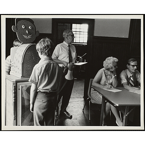 Two boys standing at the freckle meter while a staff member with a megaphone and two judges look off to their left at a Boys' Club Freckle King Contest