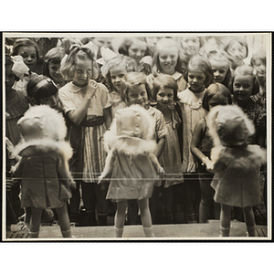 Girls looking at three dolls on display at a Boys' Club Little Sisters' Beauty Contest