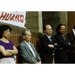 Suzanne Lee (first from left) standing next to four men, listening to a speaker at the rally for Long Guang Huang in City Hall Plaza in Boston