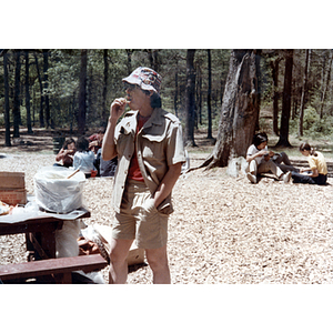 Man stands near a picnic table, while others sit and eat in the background