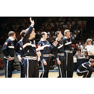 USA men's volleyball team member raises his hand above his head while standing in a line with the rest of his team