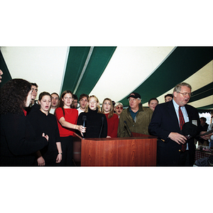 Neal Finnegan and a group of students sing behind a podium at a Harvard football game