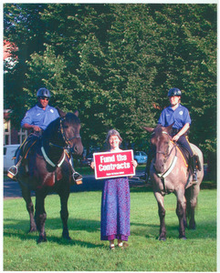 Lisa Lipshires with protest sign 'Fund the contracts,' standing between two mounted police