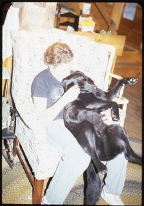 Unidentified person and black Labrador retriever seated in the living room, Wendell Farm