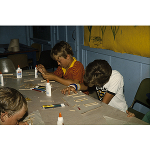 Boys seated around table making crafts with popsicle sticks